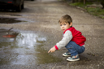 Full length of cute boy crouching by puddle