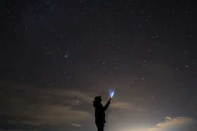Silhouette man holding illuminated flashlight while standing against star field at night