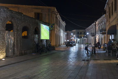 People on street amidst buildings during rainy season at night