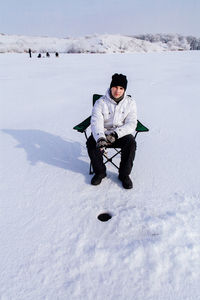 Man sitting on chair over snow field during winter