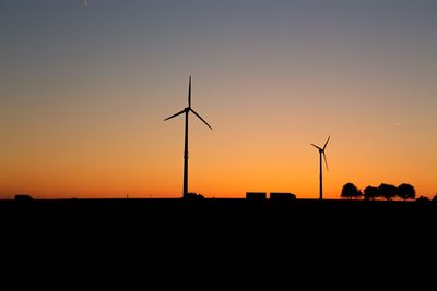 Silhouette wind turbines on field against romantic sky at sunset