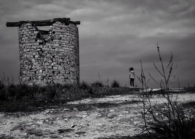 Man standing by old building on field against sky