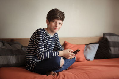 Boy teen with phone on sofa at home, real interior, concept of gadget dependency 