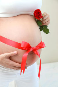 Midsection of pregnant woman with red ribbon tied on abdomen