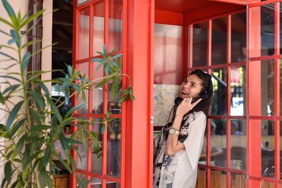 Young woman using mobile phone while standing against brick wall