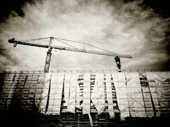 Low angle view of crane against cloudy sky