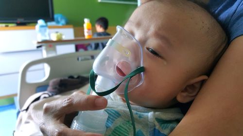 Cropped image of mother holding toddler son with oxygen mask in hospital