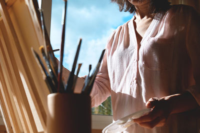 Woman painting picture on canvas at easel near the window in the studio. art painting hobby. 