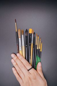 Close-up of hand holding pencils against colored background