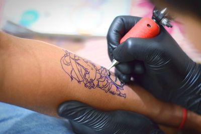 Cropped hand of artist making tattoo on customer hand