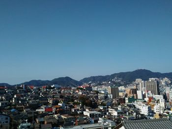 Cityscape by sea against clear blue sky