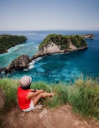 Man sitting on shore at beach against sky