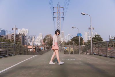 Side view of woman walking on city street against sky