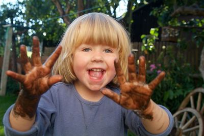 Portrait of playful girl showing messy hands while standing at backyard