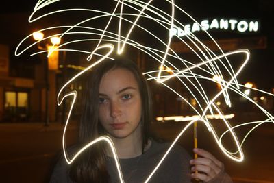 Close-up portrait of woman standing amidst light painting at night