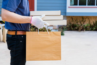 A male delivery man holds a box of goods and food for a customer in front of the house.