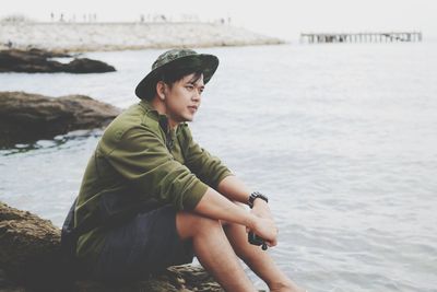 Man looking away while sitting by sea against sky