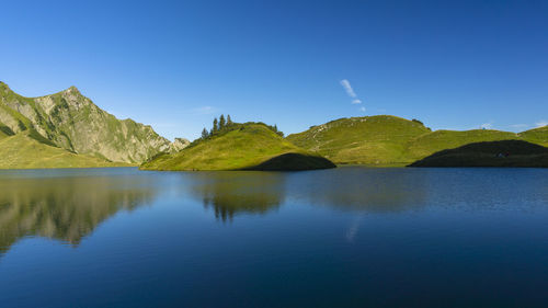 Scenic view of calm lake and mountain against blue sky