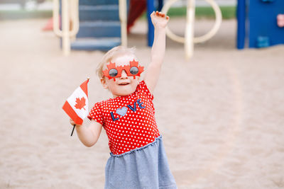 Portrait of cute girl wearing sunglasses while holding flag on sand