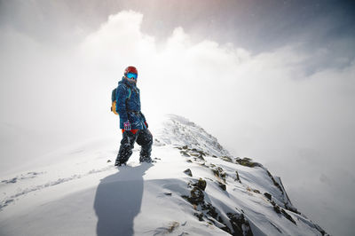Portrait of a man standing on top of a mountain, in ski clothes, blocking the sun with his back