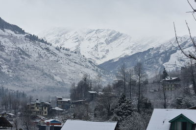 Snow covered houses by buildings against sky