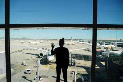 Rear view of silhouette man standing by airplane window