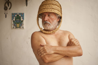 Portrait of shirtless man wearing hat standing against wall