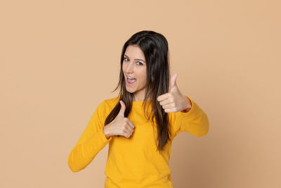 Portrait of smiling young woman standing against yellow background