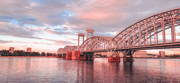 Bridge over river in city against cloudy sky