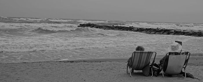 Rear view of people sitting on deck chairs at beach