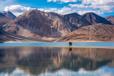 Man and woman standing at lake against mountains 