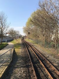 Railroad track along bare trees against clear sky