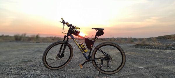 Bicycle on road amidst field against sky during sunset