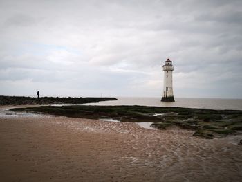 Lighthouse on beach by sea against sky