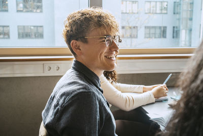 Side view of smiling young blond man wearing eyeglasses sitting in classroom