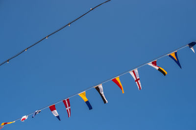 Low angle view of flags against clear blue sky