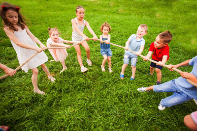 Cheerful kids playing with rope on grass outdoors