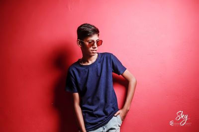 Portrait of young man standing against red wall