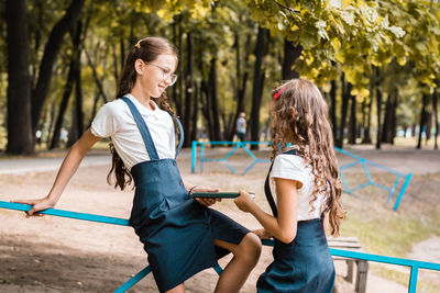 Two female students in school uniforms share a book in the park on a warm day