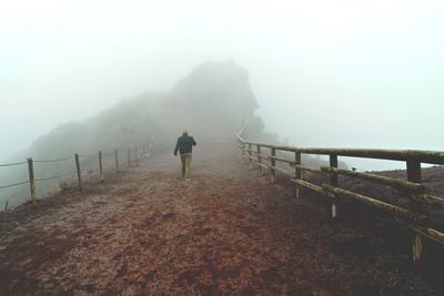 Rear view of man walking on mountain during foggy weather