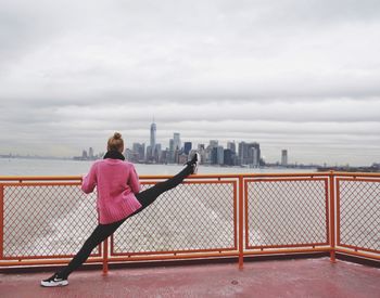 Rear view of woman on retaining wall by river against sky