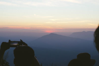 Silhouette people photographing mountains against sky during sunset