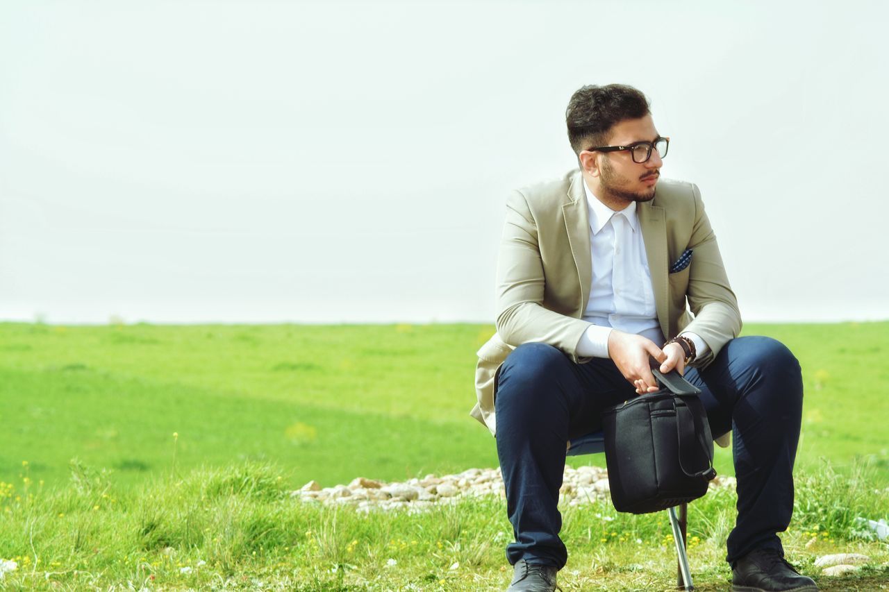 casual clothing, lifestyles, person, grass, young men, standing, leisure activity, young adult, field, three quarter length, front view, clear sky, smiling, portrait, copy space, looking at camera, grassy, happiness