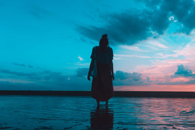 Rear view of silhouette man standing in sea against sky