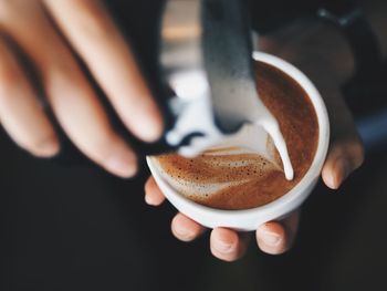 Close-up of hand pouring milk in coffee