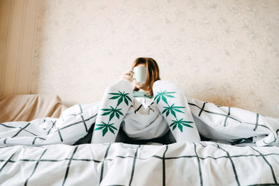 Woman sitting on bed against wall