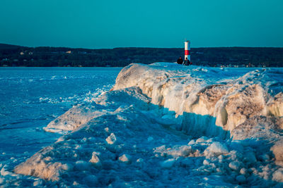 Lighthouse amidst sea and buildings against sky