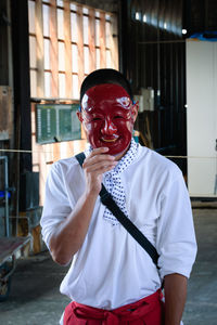 Portrait of man holding red while standing against wall