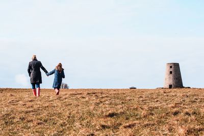 Mother and daughter walking on field against sky