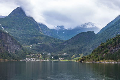 Scenic view of lake by mountains against cloudy sky at geirangerfjord